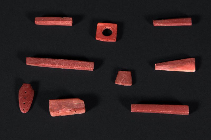 Eight pieces of catlinite that have been fashioned into beads and pendants.